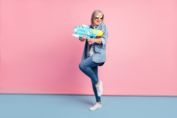 Full length photo of funny aged lady go play water gun wear jeans shirt isolated on pink background
