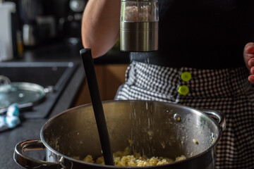 a woman in her home kitchen seasoning the stuffing in a large silver pot