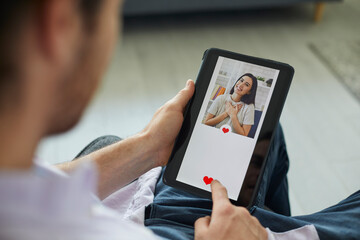 Finding love on modern online dating website or mobile app: Man looking at profile pic of pretty young woman on digital tablet display gives her like and sends her message. Close up, closeup shot - obrazy, fototapety, plakaty