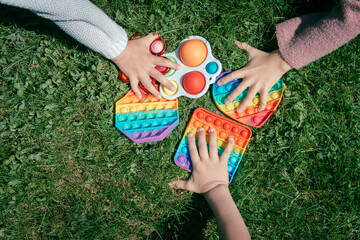 Children pull hands to pop it toys laying on green grass