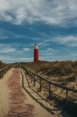 Fototapeta na wymiar Red lighthouse on texel island wooden railing near the footpath blue sky, white clouds, background, general plan, vertical