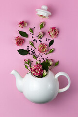 Creative layout with flowers flying out of the teapot. Kettle and roses. Pink background. View from above. Flat lay. Tea time concept.