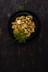 salted milk mushrooms with green sprigs of dill in a black bowl on a black wooden table with copy space top view