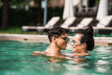 Side view of smiling couple in sunglasses relaxing in swimming pool