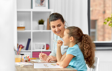 Obraz na płótnie Canvas family, hobby and leisure concept - happy smiling mother spending time with her little daughter drawing or painting wooden chipboard cutouts with colors at home
