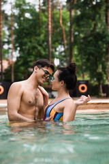 Cheerful couple hugging each other in swimming pool on blurred foreground