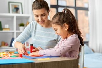 family, art and craft concept - mother spending time with her little daughter with glue making applique of color paper at home