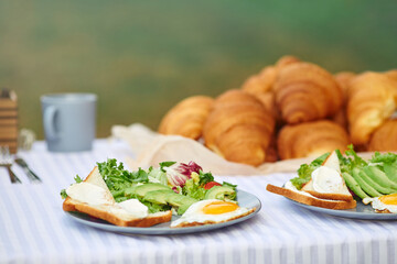Selective focus of delicious snacks for two outdoors. Close up view of beautiful table decoration, fresh salad with eggs and white bread toasts, plate with croissants nearby. Concept of cuisine, food.