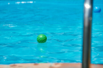 Summer image of a green rubber ball floating on the water of a pool in first term and a green one behind it ready for someone to play with them
