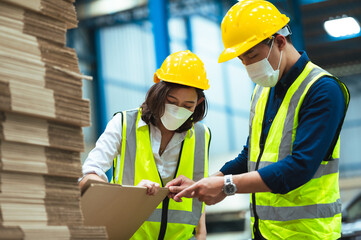 Asian male and female engineers wear protective gear and masks. Check the orderliness of the work within the warehouse.