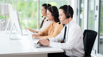 Team of call center staff in Asia wears headphones with a microphone. Smile while serving customers at desks and computers. Service concept and consulting. Communication concept.