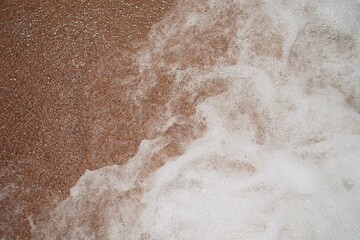 Ocean foamy wave on the sandy beach background    