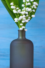 Blue background with white delicate lily of the valley flowers for mother's day vertical greeting card. Stylish modern minimal with copy space. Mockup for your design on gray glass vase.