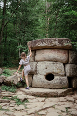 Young woman in summer dress walking near big dolmen stone in the forest