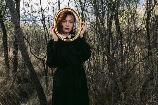 Woman in black dress looking at camera through wooden frame