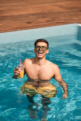 Cheerful man holding orange juice in swimming pool