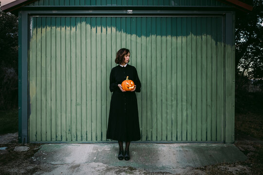 Woman with Halloween pumpkin standing near house in countryside