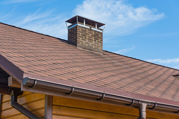 Bitumen asphalt roofing shingles and brick chimney pipe on a wooden house. Individual heating...