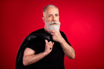 Portrait of attractive minded content fashionable grey-haired man holding leather jacket thinking isolated over bright red color background