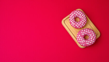 three baked round donuts in pink glaze on a red background