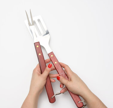 metal spatula with a wooden handle and fork for a picnic in a female hand with painted red nails on a white background
