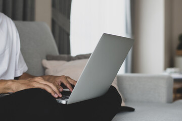 Businessman sitting on the sofa and using the laptop to check e-mails and reply to messages at home.