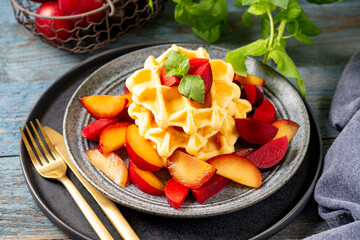 Traditional classic Belgian or Brussels waffles with red plums in a ceramic plate on a blue wooden culinary background closeup	