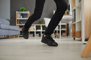 Fototapeta na wymiar Man in uncomfortable sneakers trips over power cable at home. Closeup male worker in black shoes stumbles over electric cord in office. Close up shot feet stepping on floor. Domestic accident concept