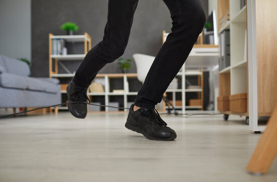 Man in uncomfortable sneakers trips over power cable at home. Closeup male worker in black shoes stumbles over electric cord in office. Close up shot feet stepping on floor. Domestic accident concept