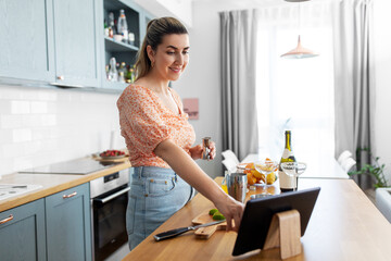 culinary and people concept - happy smiling young woman with tablet pc computer making cocktail...
