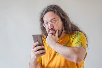 The man looks at the phone in surprise and thoughtfulness. A casually and sloppy dressed man with a...