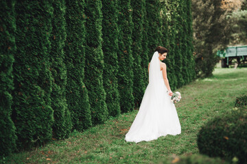 Beautiful bride in elegant white dress holding bouquet posing in park