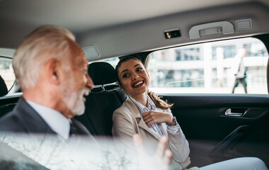 Good looking senior business man and his young woman colleague or coworker sitting on backseat in...