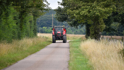 Fototapeta premium Farmer driving a red tractor a on road in the countryside.
