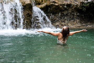 Woman swimming in the mountain river with a waterfall