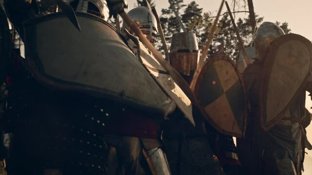 Epic Invading Army of Medieval Knights on Battlefield. Armored Soldiers in Helmets, Hit Shields with Swords in Battle Cry. War, Conquest, Crusade. Historical Reenactment. Cinematic Tracking Shot