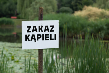Closeup of &ldquo;Zakaz kąpieli&rdquo; (English &ldquo;No swimming&rdquo;) sign at a pond in a city park.