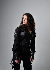 Close up portrait of young woman with natural brown hair,  wearing black leather scifi outfit with corset, standing pose on light grey studio background.