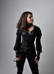 Close up portrait of young woman with natural brown hair,  wearing black leather scifi outfit with corset, standing pose on light grey studio background.