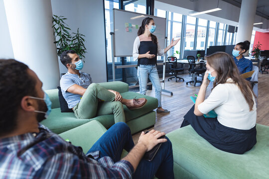 Diverse group of creative colleagues wearing face masks talking at meeting - Powered by Adobe
