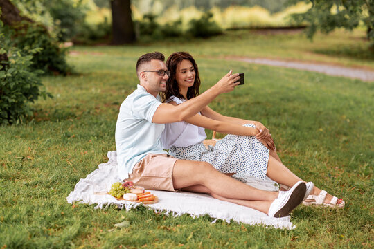 leisure and people concept - happy couple having picnic and taking selfie with smartphone at summer park