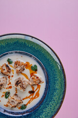 Cream cheese soup with croutons in a blue plate isolated on a pink background. Space for text. Photo for menu and site.