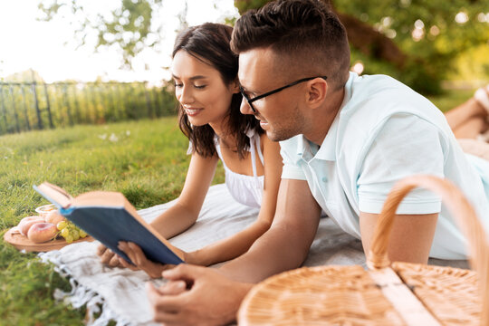 leisure, vacation and people concept - happy couple lying on picnic blanket at summer park and reading book together