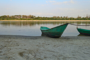 A rusty iron boat is chained on the evening bank of the river.   