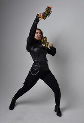 Full length portrait of young woman with natural brown hair,  wearing black leather scifi outfit with corset, standing pose on light grey studio background.