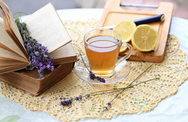 Obraz na płótnie Canvas Lavender tea in a glass cup, a bouquet of lavender in an open book, and sliced ripe lemons. Healthy and relaxing leisure concept. Soothing tea for a good sound sleep