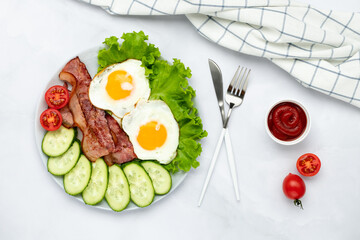 Fried eggs with bacon and vegetables on a gray table, food background in morning. Fresh cucumbers and tomatoes. Breakfast concept. Top view. Flat lay composition.