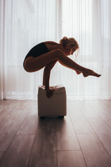 A beautiful girl in a sports swimsuit is doing yoga, practicing different asanas on a cube