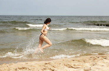 young beautiful girl running along the sand of the sea shore