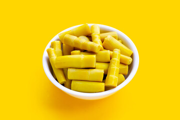 Preserved bamboo shoot in white bowl on yellow background.